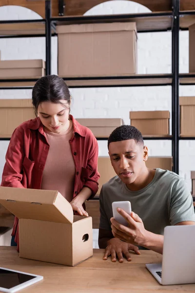 Vendedores interraciales que utilizan dispositivos y cajas de cartón en la tienda online - foto de stock