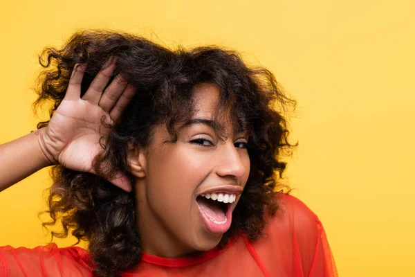 Étonnante femme afro-américaine montrant un geste d'ouïe insaisissable isolé sur jaune — Photo de stock