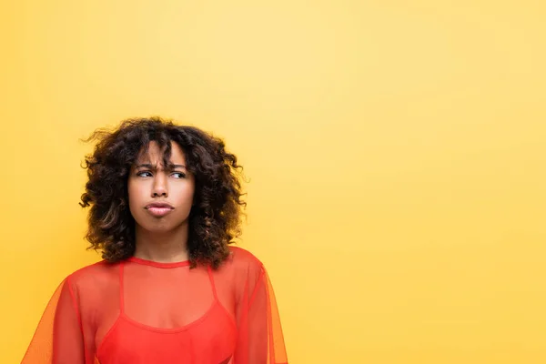 Offended african american woman in red top pouting lips and looking away isolated on yellow — Stock Photo