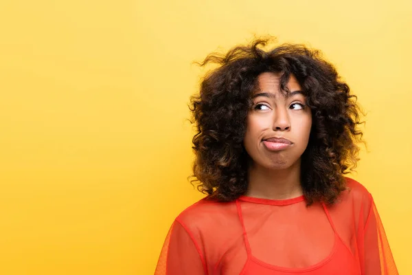 Thoughtful african american woman grimacing and looking away isolated on yellow — Stock Photo