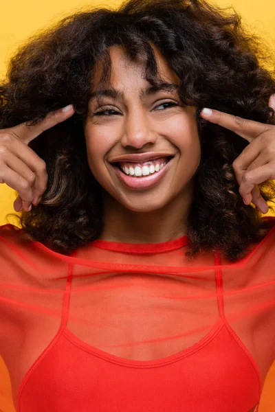 Радостная африканская американка, указывающая пальцами на глаза, изолированные на желтом — стоковое фото