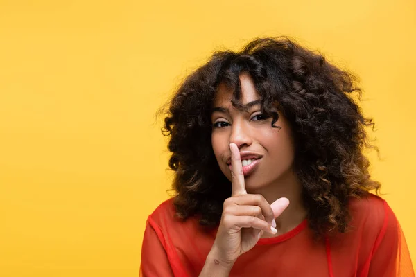 Smiling african american woman showing hush sign and looking at camera isolated on yellow — Stock Photo