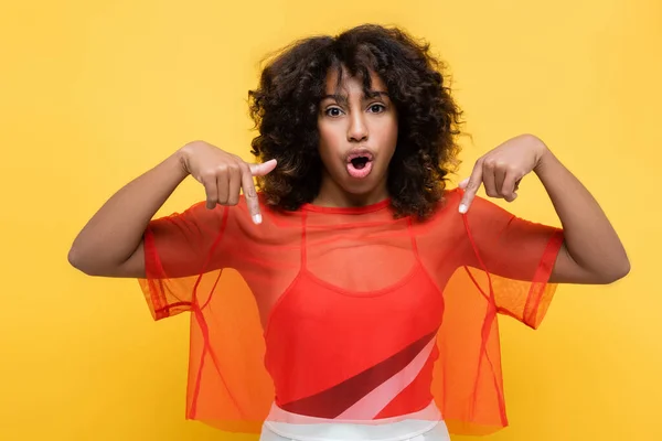 Amazed african american woman in stylish summer outfit pointing down with fingers isolated on yellow — Stock Photo