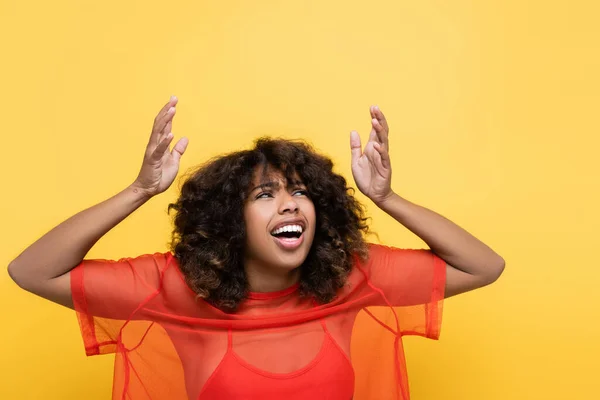 Shocked african american woman in red clothes looking up and pointing with hands isolated on yellow — Stock Photo