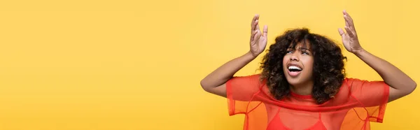 Thrilled african american woman in red top pointing up with hands isolated on yellow, banner — Stock Photo