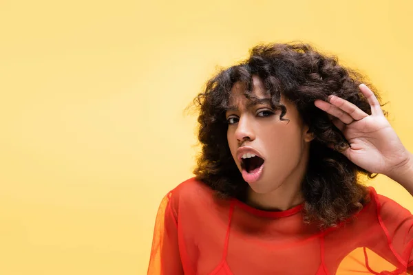 Astonished african american woman showing listening gesture isolated on yellow — Stock Photo