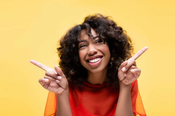 Positive african american woman with curly hair pointing with fingers isolated on yellow — Stock Photo