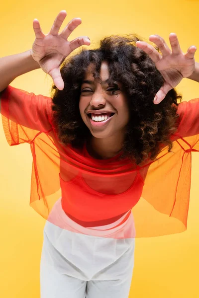 Cheerful african american woman in summer clothes showing scary gesture isolated on yellow — Stock Photo