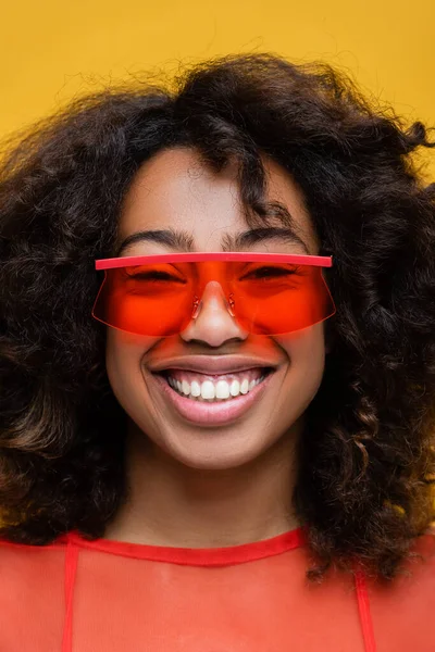 Ritratto di sorridente donna afroamericana bruna in eleganti occhiali da sole isolati sul giallo — Foto stock