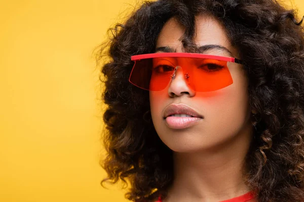 Retrato de mulher morena em óculos de sol elegantes olhando para a câmera isolada no amarelo — Fotografia de Stock