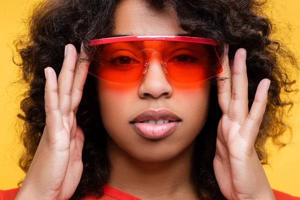 Портрет афроамериканки, що регулює модні сонцезахисні окуляри ізольовані на жовтому — стокове фото