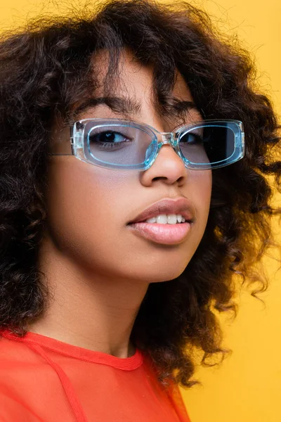 Portrait of pretty african american woman in blue and trendy sunglasses isolated on yellow — Stock Photo