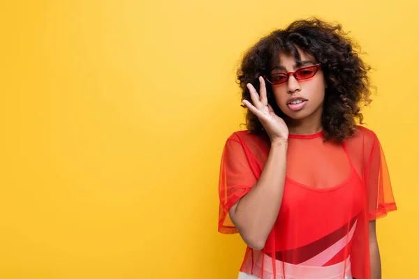 Mujer afroamericana de moda en top rojo ajustando gafas de sol aisladas en amarillo - foto de stock