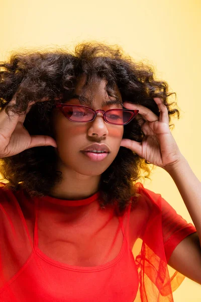 Femme afro-américaine à la mode avec les cheveux ondulés tenant la main près du visage isolé sur jaune — Photo de stock