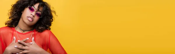 Афроамериканська жінка в стильних сонцезахисних окулярах торкається грудей і дивиться на камеру ізольовану на жовтому прапорі — стокове фото