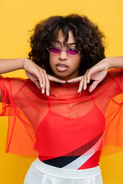 Femme afro-américaine à la mode avec les cheveux ondulés tenant la main près du visage et regardant loin isolé sur jaune — Stock Photo