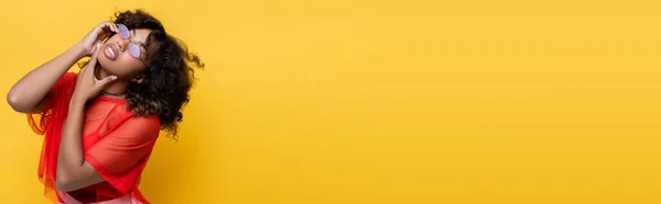 Стильная африканская американка в солнечных очках касаясь подбородка изолированы на желтый, баннер — стоковое фото