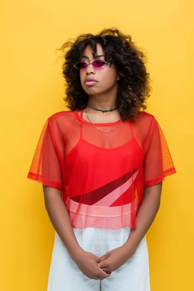 Curly african american woman in trendy sunglasses and summer outfit isolated on yellow — Stock Photo