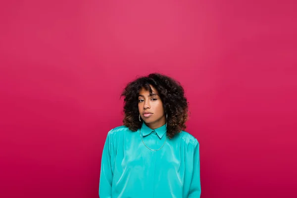 Curly african american woman in turquoise blouse looking at camera isolated on pink — Stock Photo