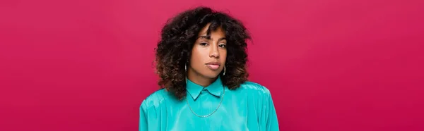 Brunette african american woman in cyan blouse looking at camera isolated on pink, banner — Stock Photo