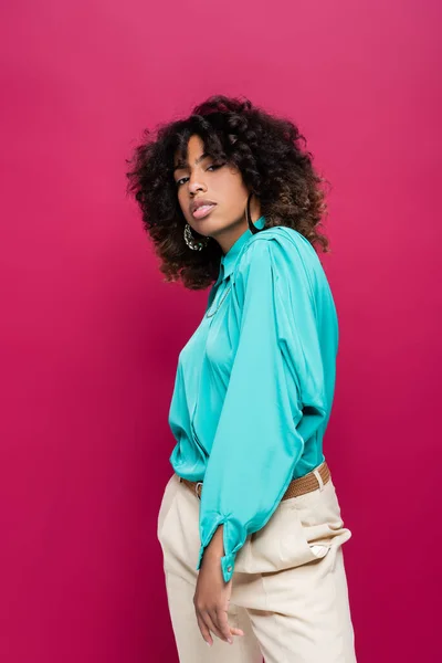 Stylish african american woman in cyan blouse looking at camera while posing isolated on pink — Stock Photo