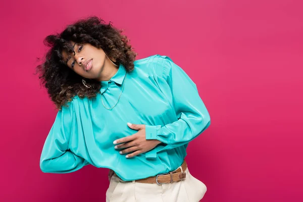 African american woman in turquoise blouse posing with hand behind back isolated on pink — Stock Photo