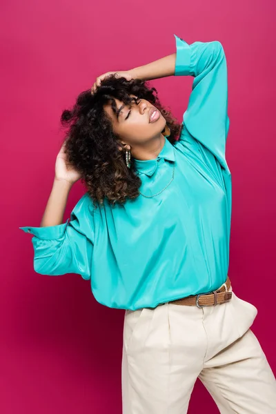 Morena afroamericana americana mujer con los ojos cerrados tocando el pelo y posando aislado en rosa - foto de stock