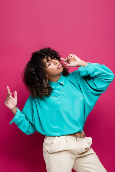 Trendy african american woman in turquoise blouse pointing with fingers isolated on pink — Stock Photo