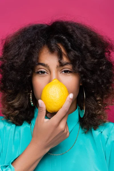 African american woman with wavy hair obscuring face with lemon isolated on pink — Stock Photo