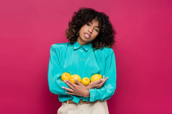 African american woman in turquoise blouse holding fresh lemons isolated on pink — Stock Photo