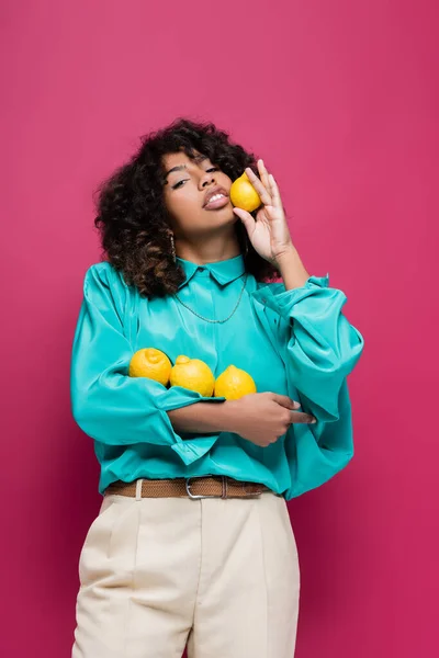 Pretty african american woman in trendy blouse holding lemons isolated on pink — Stock Photo