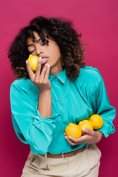 African american woman with closed eyes smelling fresh lemon isolated on pink — Stock Photo