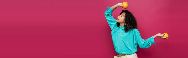 Mulher americana africana elegante em blusa azul posando com laranjas isoladas em rosa, banner — Fotografia de Stock