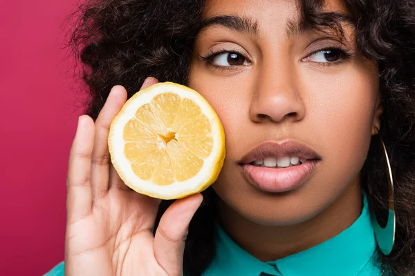 Primer plano retrato de mujer afroamericana con medio limón aislado en rosa - foto de stock