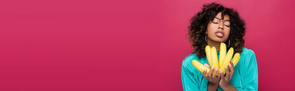 Sensual african american woman with closed eyes holding ripe bananas isolated on pink, banner — Stock Photo