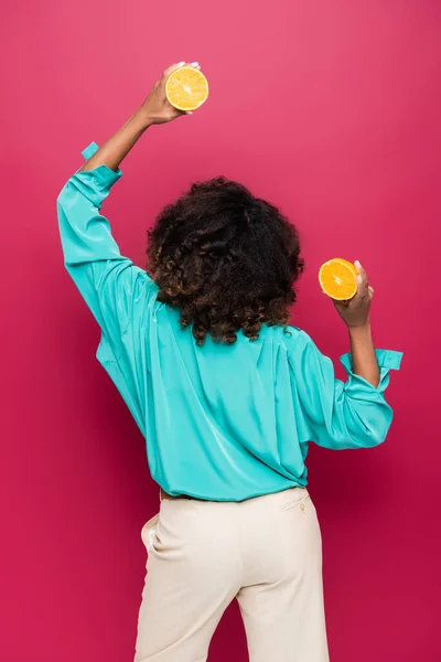 Visão traseira da mulher americana africana posando com metades de laranja madura isolada em rosa — Fotografia de Stock