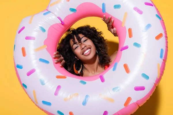 Brunette afro-américaine souriant à la caméra à travers anneau de natation sur fond jaune — Photo de stock