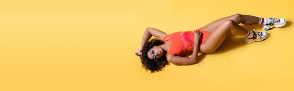 Vue du dessus de la femme brune afro-américaine en tenue de plage couchée sur fond jaune, bannière — Photo de stock