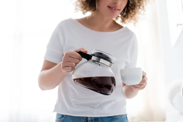 Обрезанный вид на кудрявую женщину в белой футболке, наливающую утренний кофе — стоковое фото