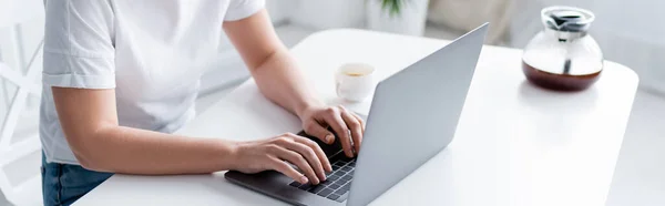 Cropped view of woman typing on laptop near cup and coffee pot, banner — Stock Photo