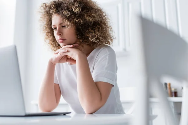 Thoughtful woman with clenched hands sitting near laptop on blurred foreground — Stock Photo