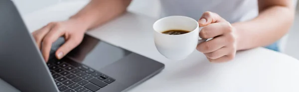 Partial view of woman holding coffee cup and typing on laptop, banner — Stock Photo