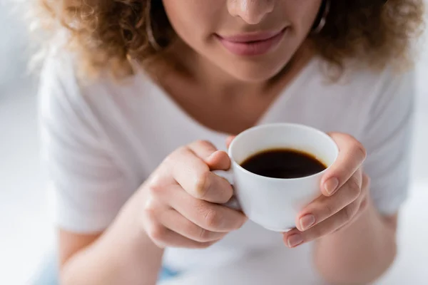 Vue recadrée de femme heureuse tenant tasse de café aromatique noir sur fond flou — Photo de stock