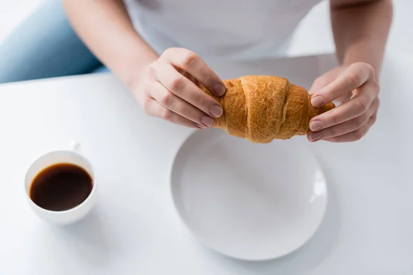 Partial view of woman holding tasty croissant near cup of black coffee — Stock Photo
