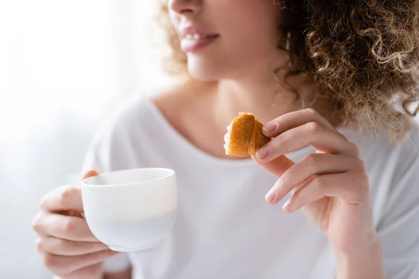 Частичный вид размытой женщины с чашкой кофе и кусочком вкусного круассана — стоковое фото