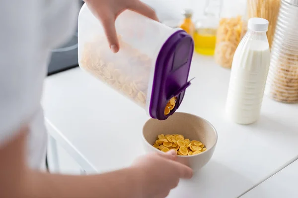 Vista recortada de la mujer vertiendo copos de maíz en un tazón cerca de la botella de leche — Stock Photo