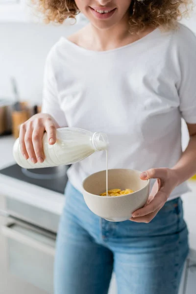 Vista parziale di donna sorridente versando latte in ciotola con gustosi corn flakes — Foto stock