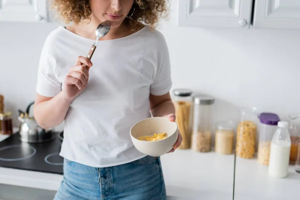 Частковий вигляд кучерявої жінки в білій футболці, що тримає ложку і миску з кукурудзяними пластівцями — стокове фото