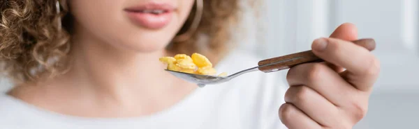 Teilansicht der lockigen Frau, die einen Löffel mit leckeren Cornflakes hält, Banner — Stockfoto