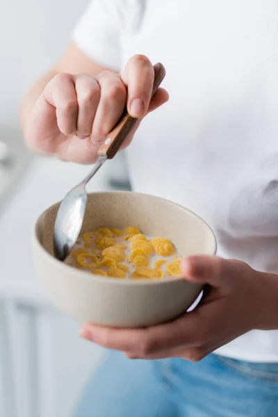 Vista parziale della donna che tiene cucchiaio e ciotola di fiocchi di mais con latte — Foto stock